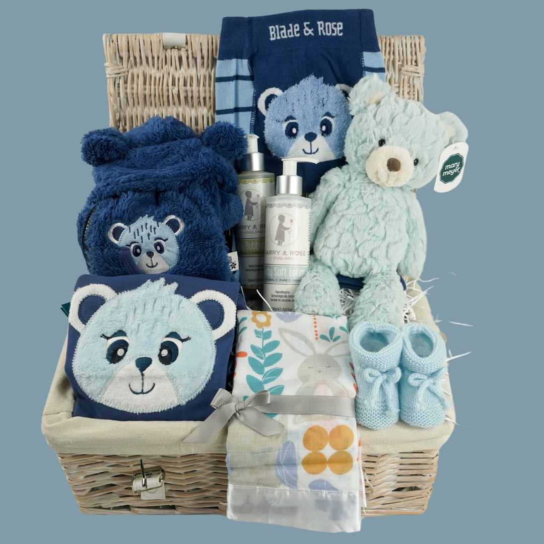 white hamper basket with baby boy gifts, Blade & Rose baby t-shirt with long sleeves in navy with applique teddy, striped navy leggings with teddy on the bum, organic toiletries, blue soft teddy bear, blue baby booties, baby swaddle with rabbits and owl