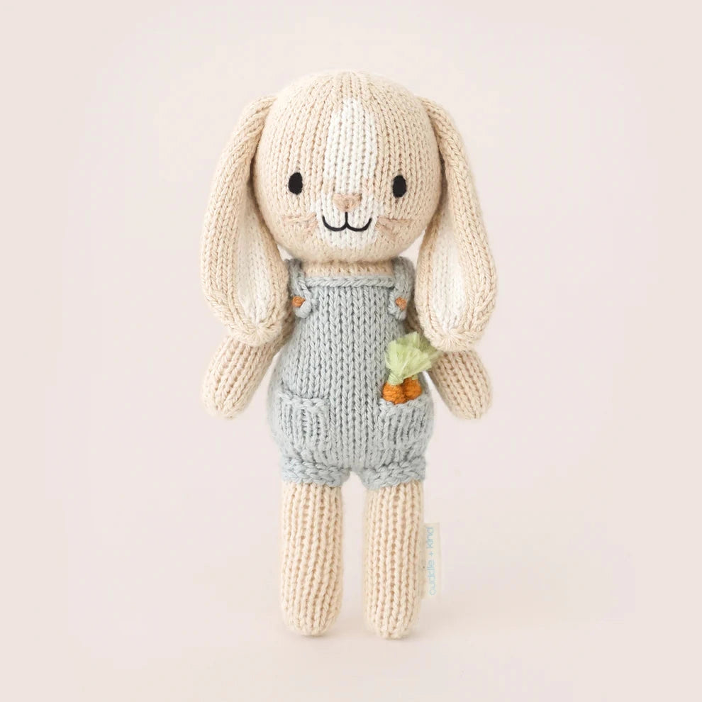 Knitted toy rabbit with a carrot in his pocket and light blue dungarees