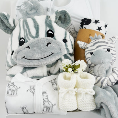 white hamper box with baby dressing gown with zebra faced hood, white baby sleepsuit with zebras, white baby hat with zebras, grey and white baby comforter with a zabra head, white knit baby booties, black and white sensory muslin swaddle and