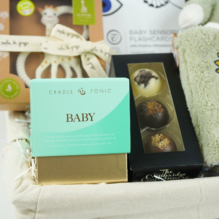 White hamper basket with baby sensory muslin, baby sensory flash cards, Sophie la Giraffe teether, Miffy soft toy, Miffy soft activity book in Green, Aromatherapy candle, chocolates