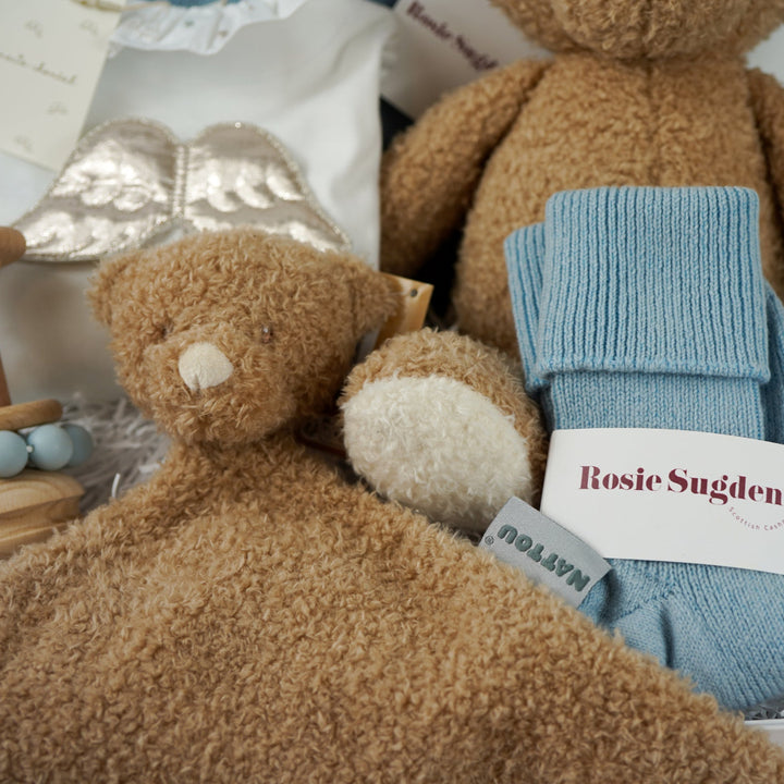 Luxury baby gift hamper box with pale blue cashmere baby cardigan, white luxury baby sleepsuit with frilled collar and silver angel wings on the back, wooden baby rattle with blue silicone teething beads, matching cashmere socks for mum in pal blue, soft teddy and matching baby comforter