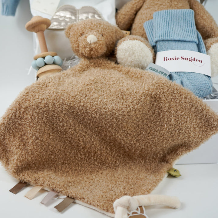 Luxury baby gift hamper box with pale blue cashmere baby cardigan, white luxury baby sleepsuit with frilled collar and silver angel wings on the back, wooden baby rattle with blue silicone teething beads, matching cashmere socks for mum in pal blue, soft teddy and matching baby comforter
