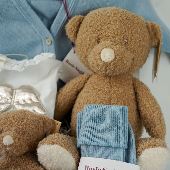 Luxury baby gift hamper box with pale blue cashmere baby cardigan, white luxury baby sleepsuit with frilled collar and silver angel wings on the back, wooden baby rattle with blue silicone teething beads, matching cashmere socks for mum in pal blue, soft teddy and matching baby comforter
