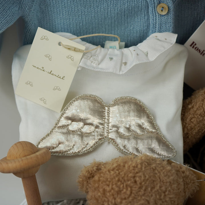 Luxury baby gift hamper box with pale blue cashmere baby cardigan, white luxury baby sleepsuit with frilled collar and silver angel wings on the back, wooden baby rattle with blue silicone teething beads, matching cashmere socks for mum in pal blue, soft teddy and matching baby comforter