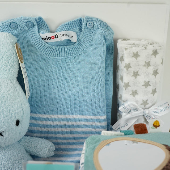 baby boy hamper with blue fine knit romper with white striped and pocket, white muslin with silver stars, blue terry miffy, Forest friends Fox soft activity book, blue knit booties, chocolate stirrer spoon with mini eggs