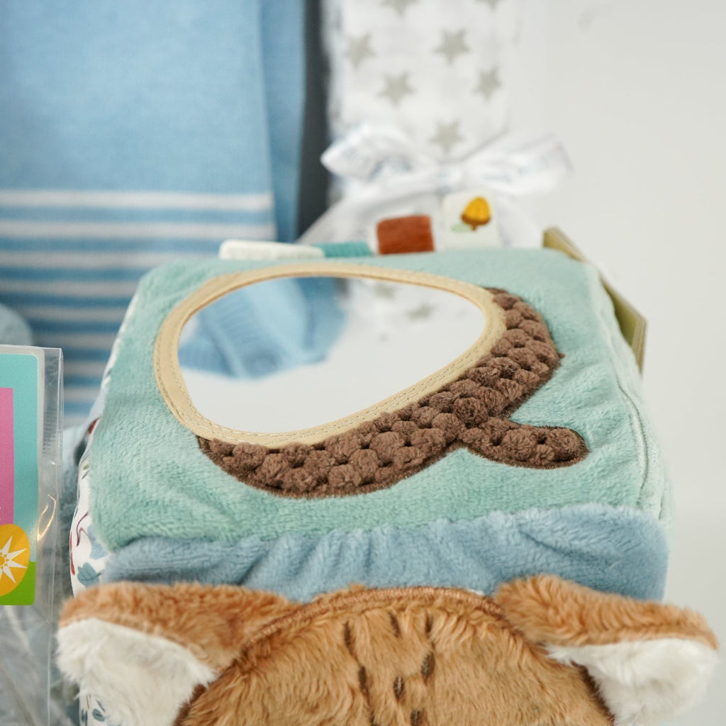 baby boy hamper with blue fine knit romper with white striped and pocket, white muslin with silver stars, blue terry miffy, Forest friends Fox soft activity book, blue knit booties, chocolate stirrer spoon with mini eggs