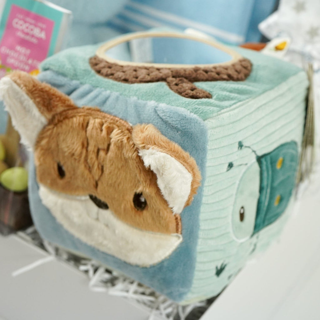baby boy hamper with blue fine knit romper with white striped and pocket, white muslin with silver stars, blue terry miffy, Forest friends Fox soft activity book, blue knit booties, chocolate stirrer spoon with mini eggs