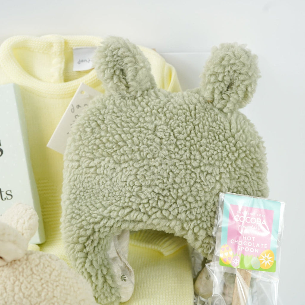 easter baby hamper, yellow knit romper with bunny design and pompom tail, soft fluffy bunny ears green hat with matching bunny ears , booties , recycled cream bunny cuddle toy, miles and moments baby cards, hot chocolate spoon with small eggs