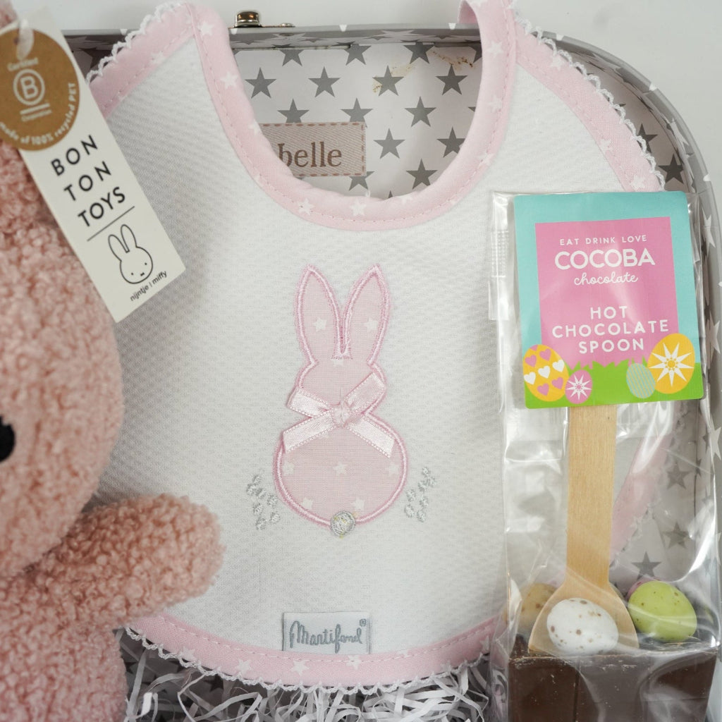 baby keepsake trunk with pink Miffy teddy, white bib with pink scalloped edge and applique bunny design , matching white wrap with pink edging and bunny applique design, pink booties , chocolate sppon with easter eggs