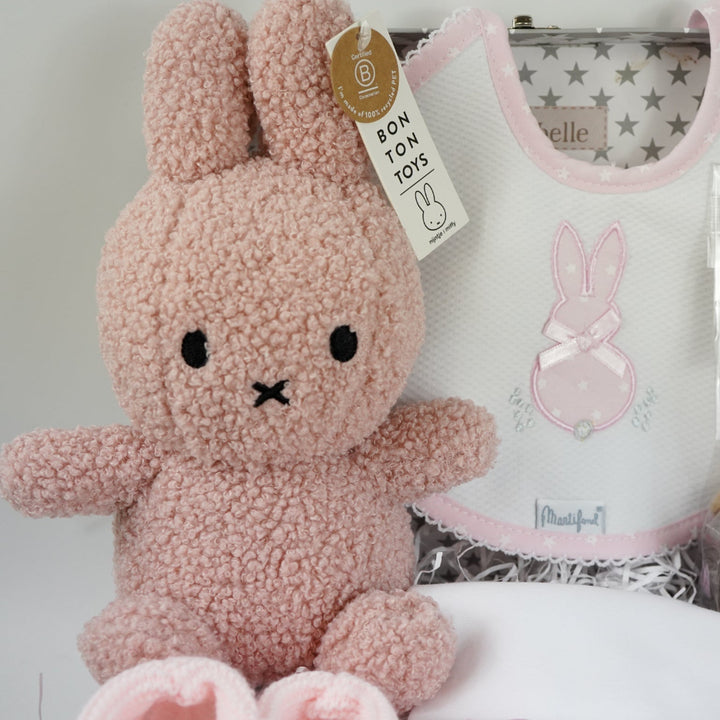 baby keepsake trunk with pink Miffy teddy, white bib with pink scalloped edge and applique bunny design , matching white wrap with pink edging and bunny applique design, pink booties , chocolate sppon with easter eggs