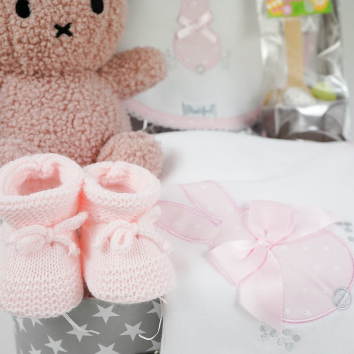 baby keepsake trunk with pink Miffy teddy, white bib with pink scalloped edge and applique bunny design , matching white wrap with pink edging and bunny applique design, pink booties , chocolate sppon with easter eggs