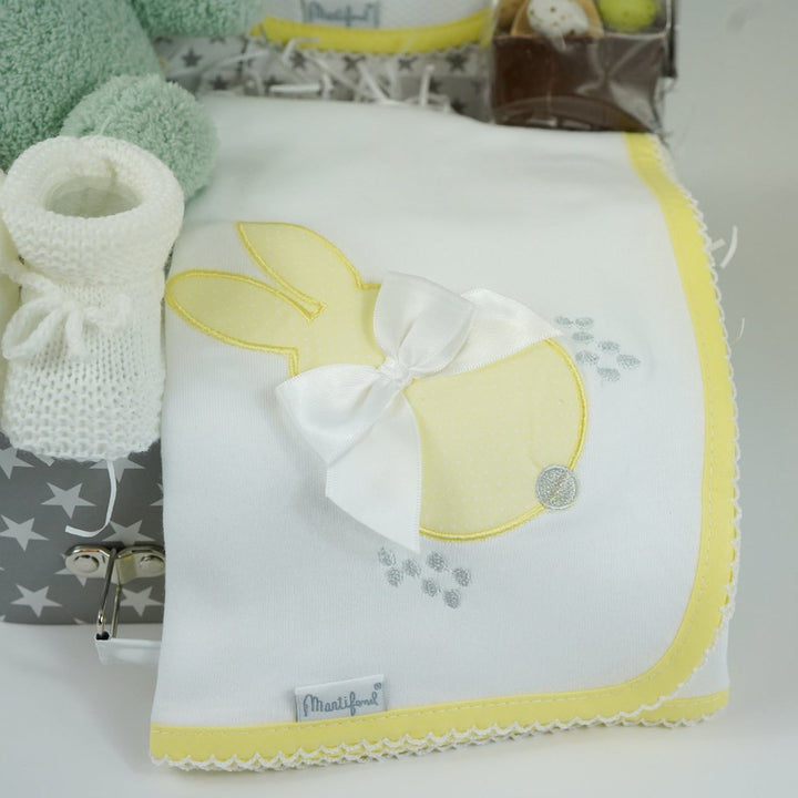 baby keepsake case with green miffy bunny, white bib with yellow scalloped edging and applique bunny with a bow and matching wrap, white baby knit booties , chocolate spoon with mini eggs
