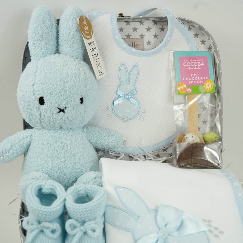 baby case with Blue miffy bunny, white and pale blue baby bib with applique bunny with a ribbon, white wrap with blue applique bunny with ribbon bow, blue knit booties