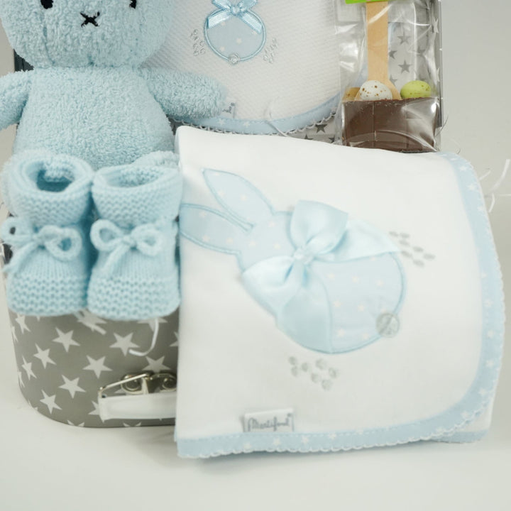 baby case with Blue miffy bunny, white and pale blue baby bib with applique bunny with a ribbon, white wrap with blue applique bunny with ribbon bow, blue knit booties