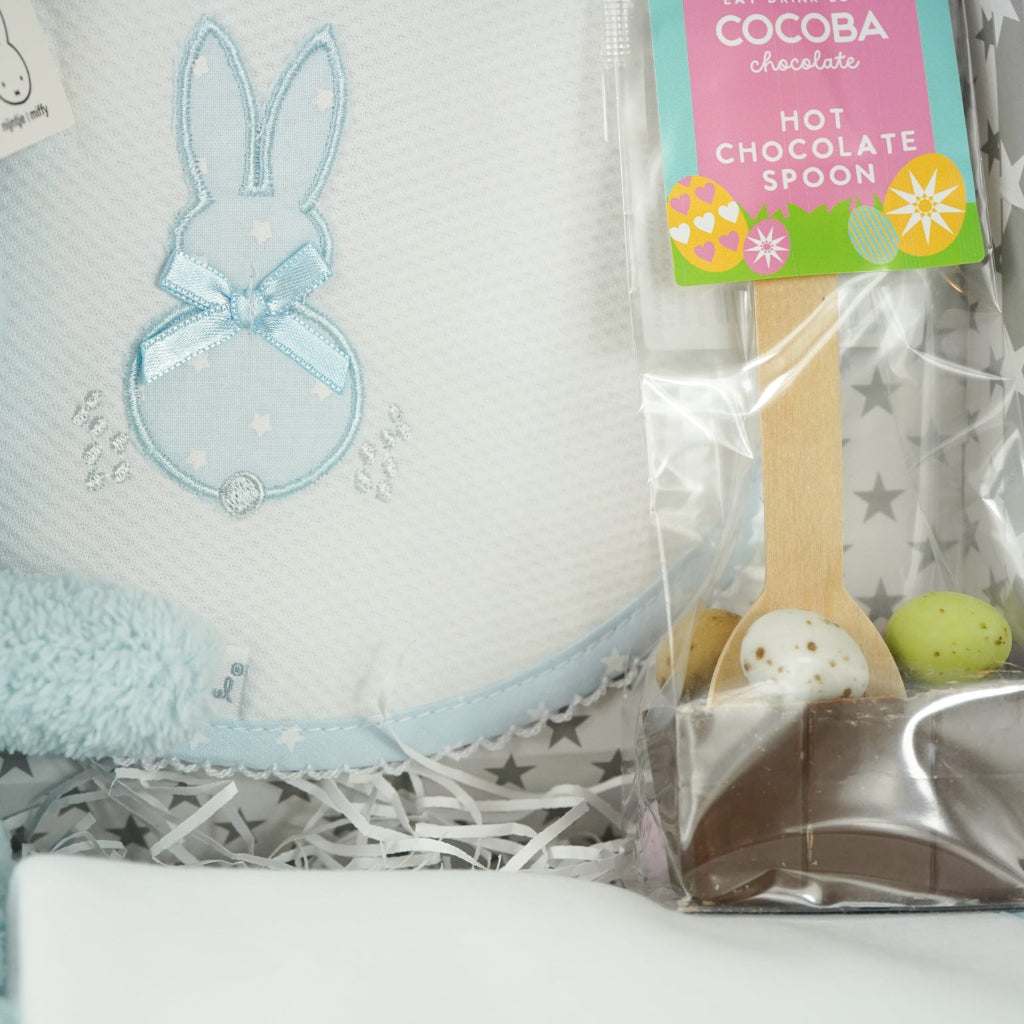 baby case with Blue miffy bunny, white and pale blue baby bib with applique bunny with a ribbon, white wrap with blue applique bunny with ribbon bow, blue knit booties