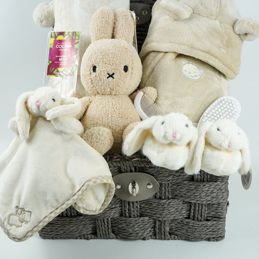 neutral baby gift hamper with  beige and caramel heart blanket with pompoms, baby dressing gown with cute ears, baby bunny slipper and matching bunny comforter, caramel miffy soft toy, chocolate spoon
