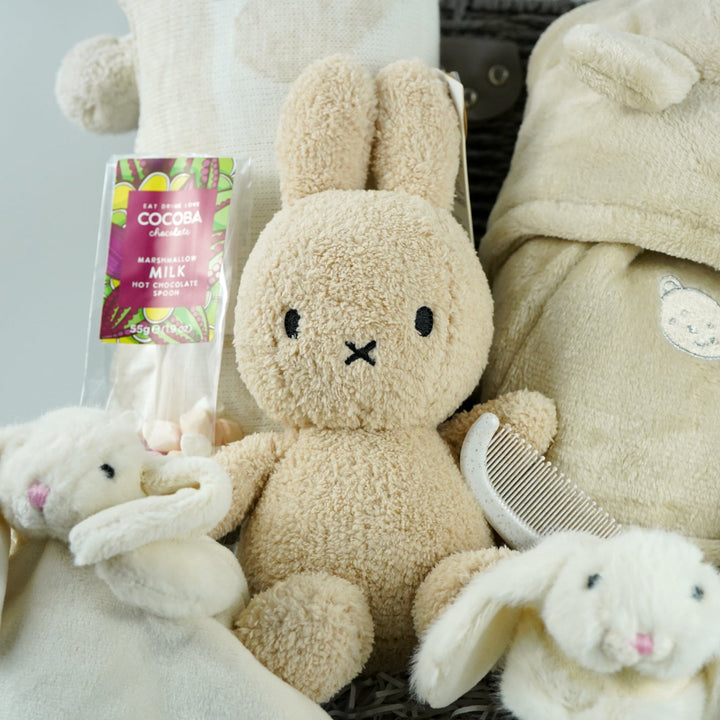 neutral baby gift hamper with  beige and caramel heart blanket with pompoms, baby dressing gown with cute ears, baby bunny slipper and matching bunny comforter, caramel miffy soft toy, chocolate spoon