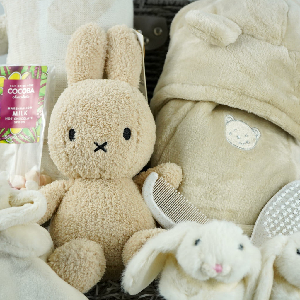 neutral baby gift hamper with  beige and caramel heart blanket with pompoms, baby dressing gown with cute ears, baby bunny slipper and matching bunny comforter, caramel miffy soft toy, chocolate spoon