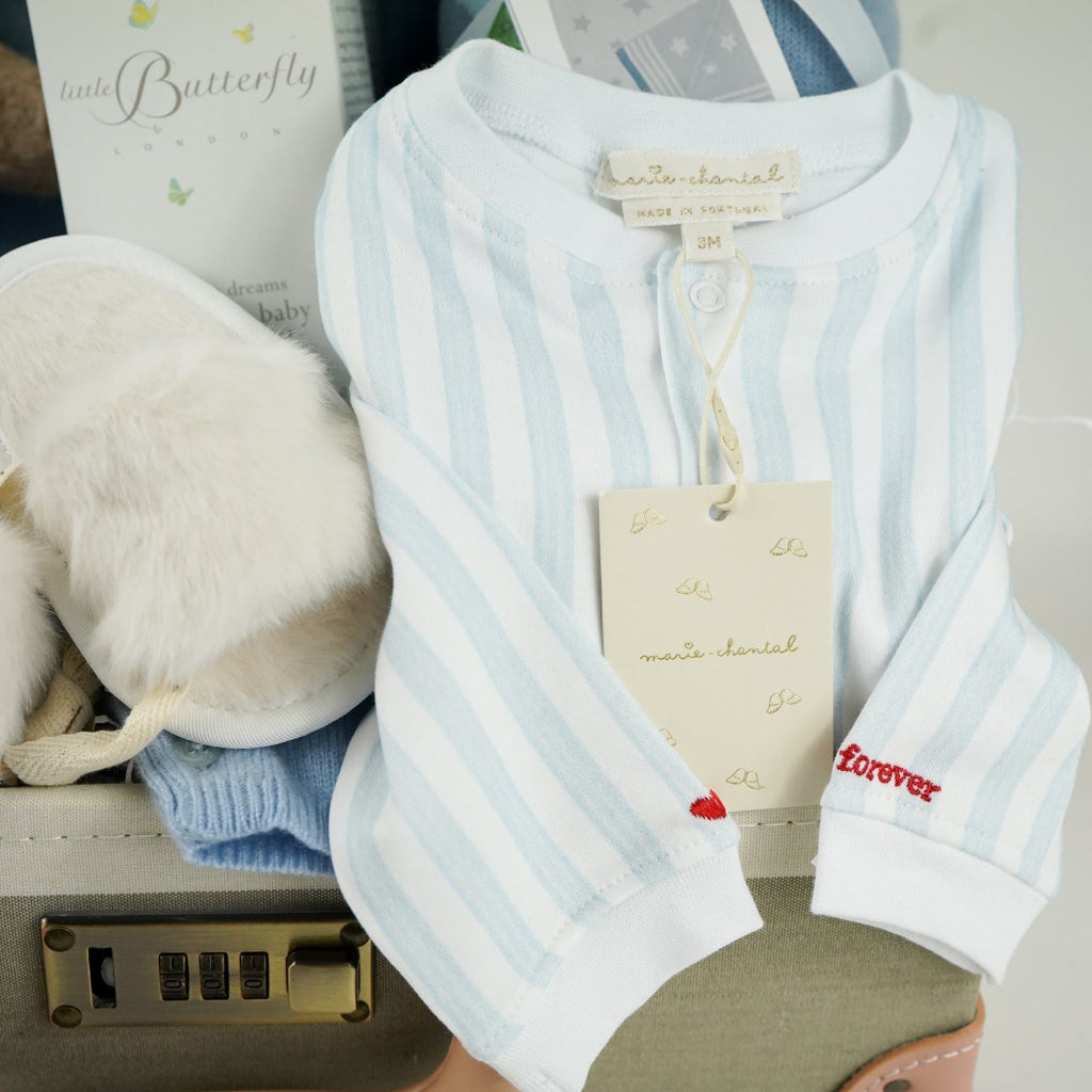 luxury baby keepsake case with luxury gifts, Steiff organic teddy with blue rompers , blue cashmere baby romper, baby toiletries organic, blue cotton blanket with star design, blue and white striped romper in organic cotton with embroidery on both sleeves, fluffy cream baby slip on slippers, wooden rattle with blue beads
