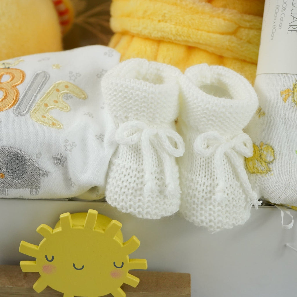 white hamper box with yellow baby dressing gown with duck face hood, soft cuddly yellow duck toy, white muslin square with yellow duck pattern., white knit baby booties, white baby sleep suit with zebra, giraffe and elephant and applique NEWBIE all in grey, yellow and orange, Early years baby journal