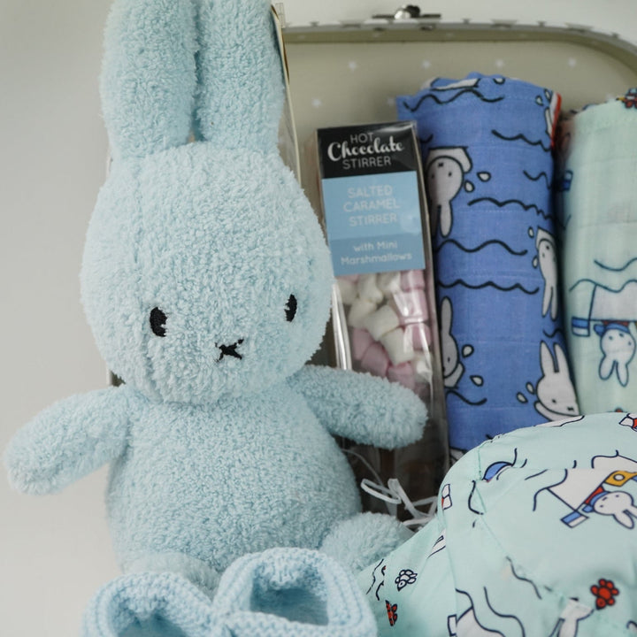 White storage suitcase with soft blue terry Miffy, pale blue knit booties with tie, salted caramel chocolate stirrer, two muslins with Miffy pattern, bucket sunhat for baby with Miffy pattern