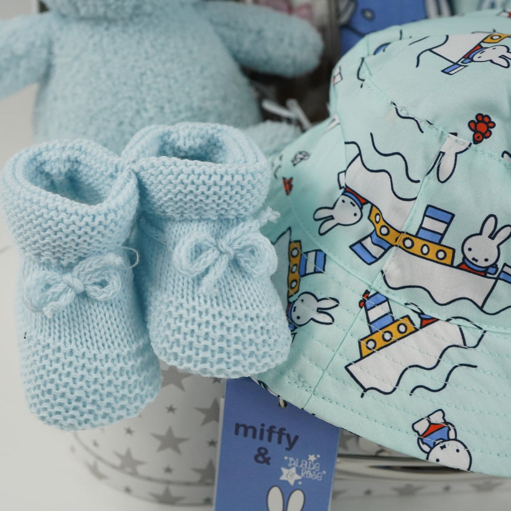 White storage suitcase with soft blue terry Miffy, pale blue knit booties with tie, salted caramel chocolate stirrer, two muslins with Miffy pattern, bucket sunhat for baby with Miffy pattern