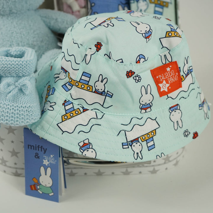 White storage suitcase with soft blue terry Miffy, pale blue knit booties with tie, salted caramel chocolate stirrer, two muslins with Miffy pattern, bucket sunhat for baby with Miffy pattern
