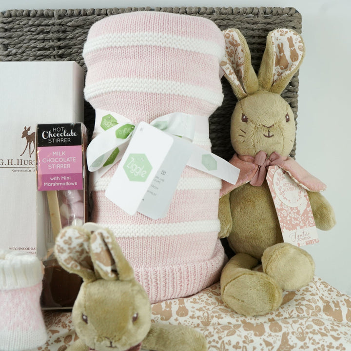 grey paper rope hamper with luxury baby brush in gift box, chocolate stirrer spoon, pink and white striped baby blanket, pink knit baby booties, peter rabbit soft toy and matching baby comforter
