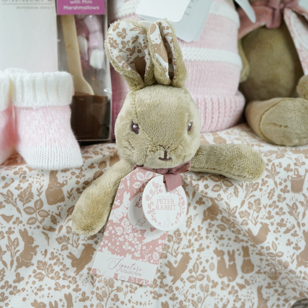 grey paper rope hamper with luxury baby brush in gift box, chocolate stirrer spoon, pink and white striped baby blanket, pink knit baby booties, peter rabbit soft toy and matching baby comforter