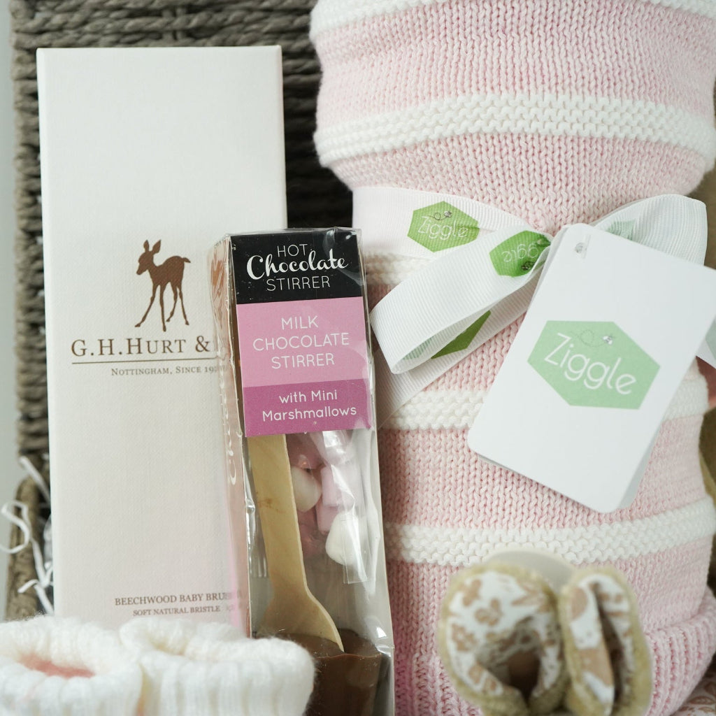 grey paper rope hamper with luxury baby brush in gift box, chocolate stirrer spoon, pink and white striped baby blanket, pink knit baby booties, peter rabbit soft toy and matching baby comforter