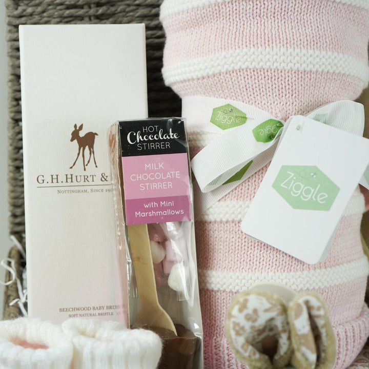 grey paper rope hamper with luxury baby brush in gift box, chocolate stirrer spoon, pink and white striped baby blanket, pink knit baby booties, peter rabbit soft toy and matching baby comforter