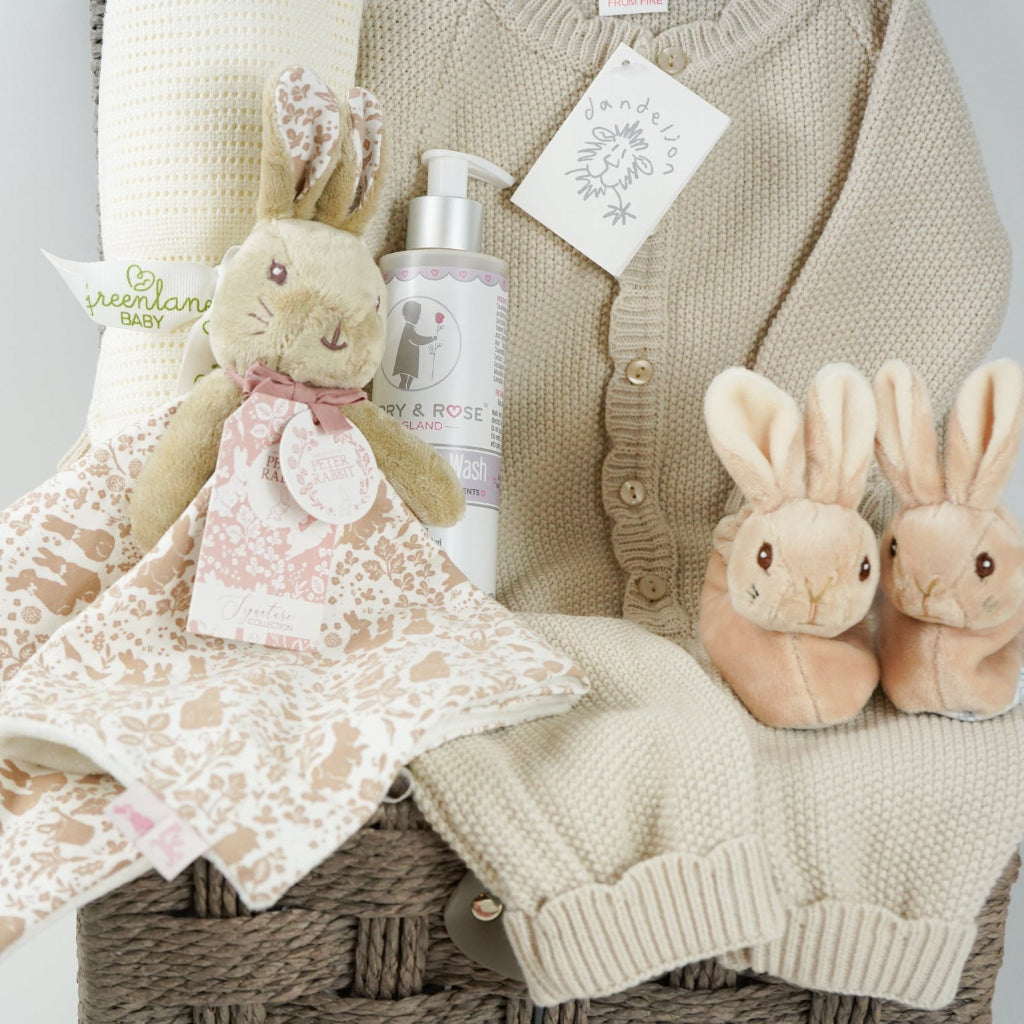 luxury baby girl hamper basket with taupe knitted romper with scalloped edges, cream cellular bamboo and cotton blanket, taupe and dusty pink flopsy bunny comforter , perter rabbit plush slippers , organic baby bubble bath