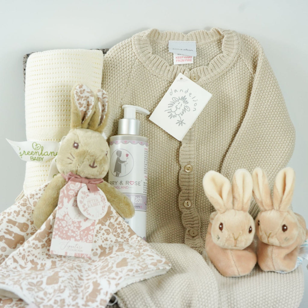 luxury baby girl hamper basket with taupe knitted romper with scalloped edges, cream cellular bamboo and cotton blanket, taupe and dusty pink flopsy bunny comforter , perter rabbit plush slippers , organic baby bubble bath