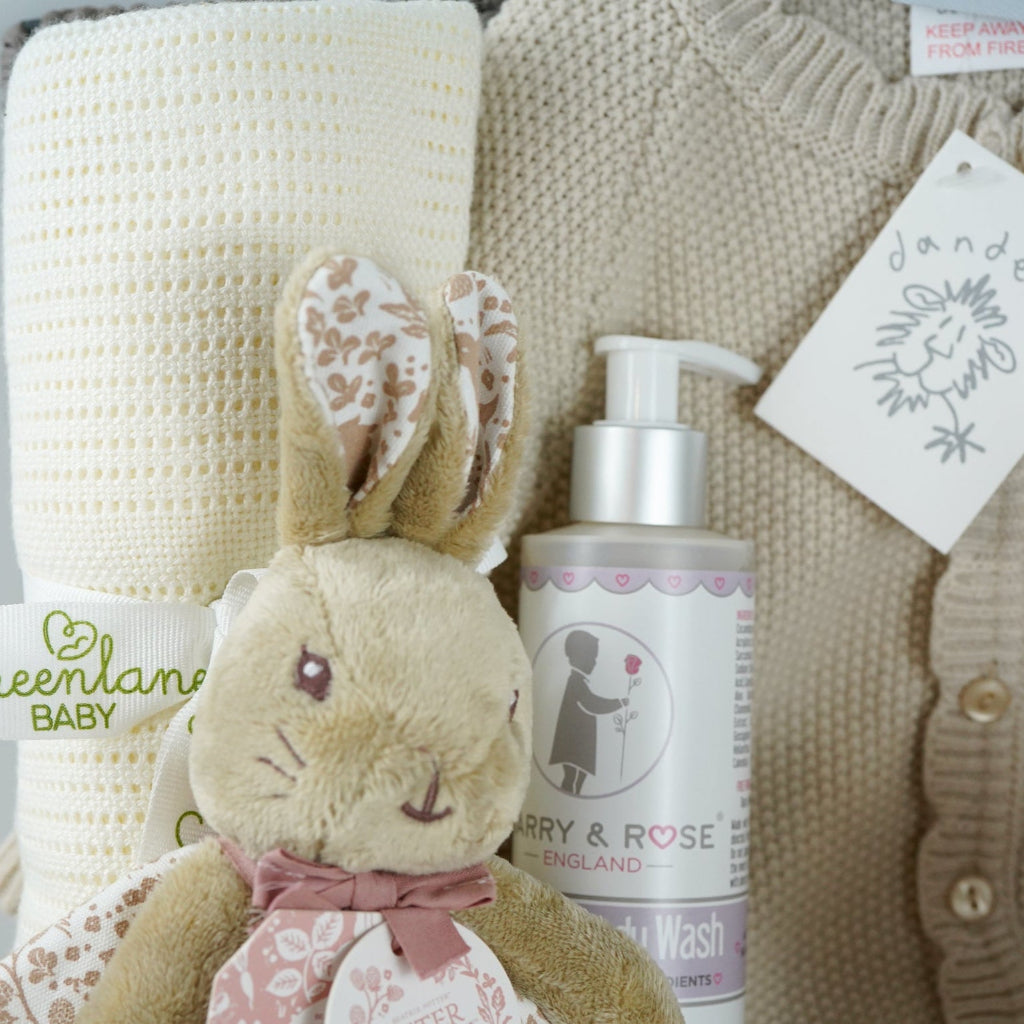 luxury baby girl hamper basket with taupe knitted romper with scalloped edges, cream cellular bamboo and cotton blanket, taupe and dusty pink flopsy bunny comforter , perter rabbit plush slippers , organic baby bubble bath