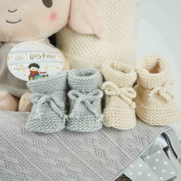 grey hamperbasket with neutral baby items including grey and cream muslin swaddles, baby toiletries, Harry Potter Dobby soft toy, grey taggie comforter , cream soft cotton baby blanket, grey booties and beige baby booties