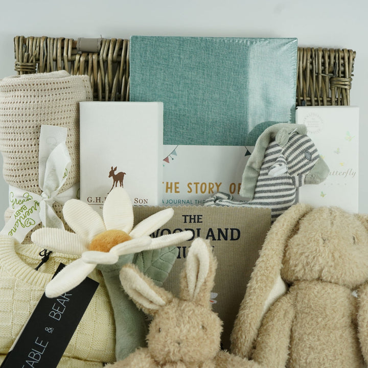 neutral baby hamper basket with caramel coloured organic cellular blanket, fabe and bear cream basket weave pattern baby 2 piece cream clothing set, bunny soft toy and matching baby comforter, luxury baby hairbrush, zebra stiped rattle, vavy diary, woodland rag book, organic baby bubble bath