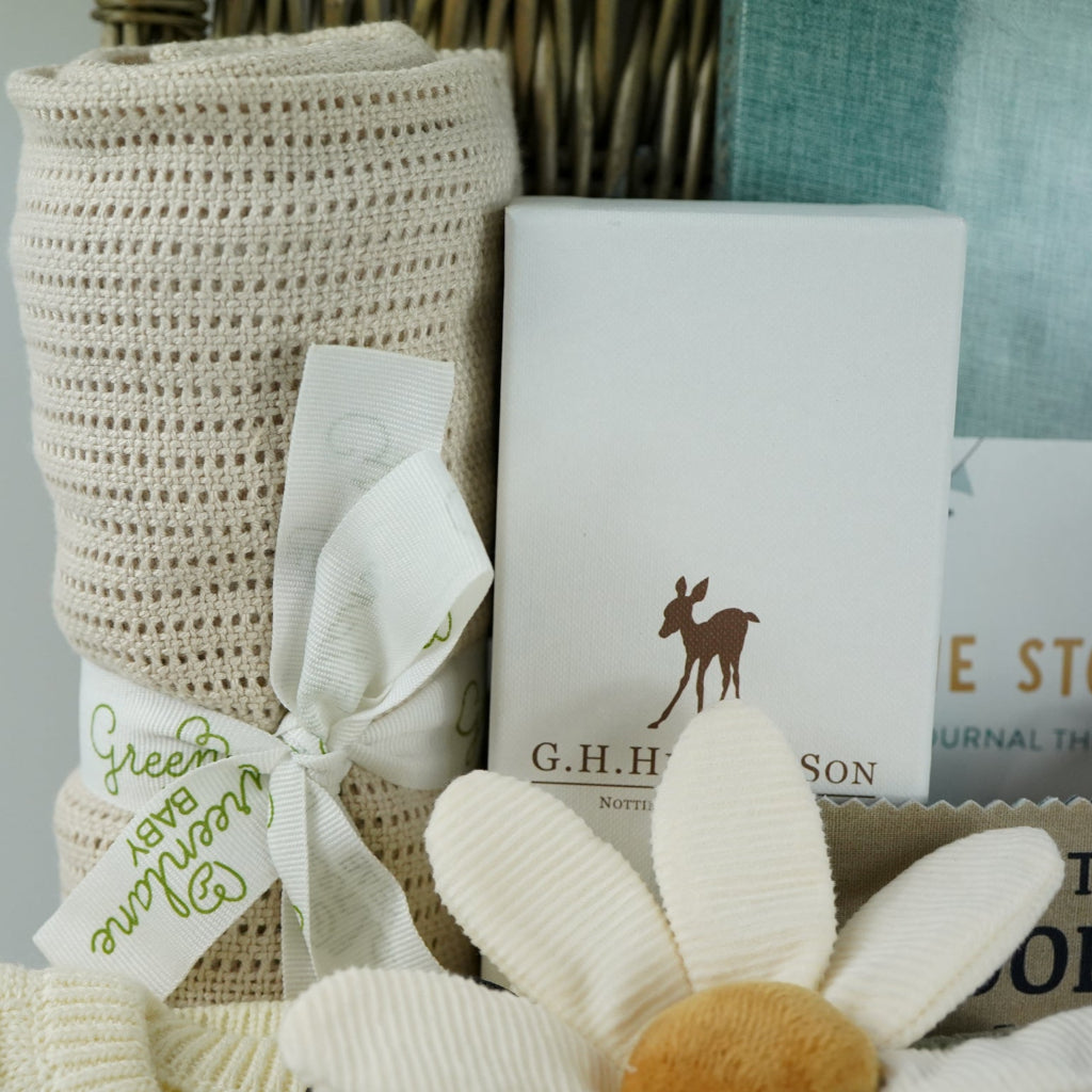 neutral baby hamper basket with caramel coloured organic cellular blanket, fable and bear cream basket weave pattern baby 2 piece cream clothing set, bunny soft toy and matching baby comforter, luxury baby hairbrush, zebra stiped rattle, baby diary, woodland rag book, organic baby bubble bath