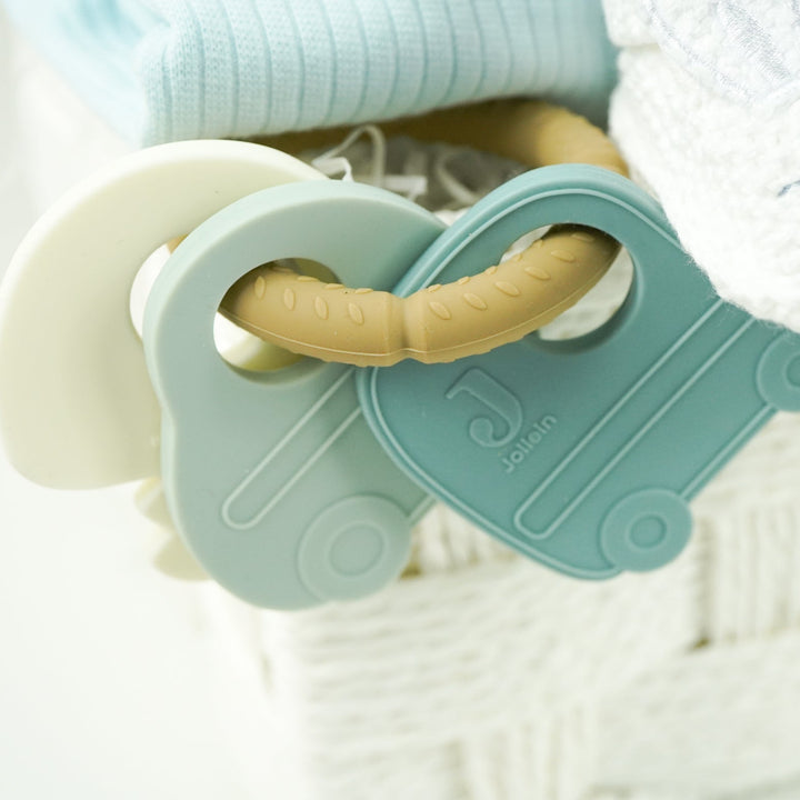 baby hamper with blue zip up baby sleepsuit, baby muslin basket in white with grey elephants, toiletries for baby, three muslins in cream with cards , car soft activity toy, white baby booties with rabbit face, silicon baby teether with 2 cars and keys in blues and cream