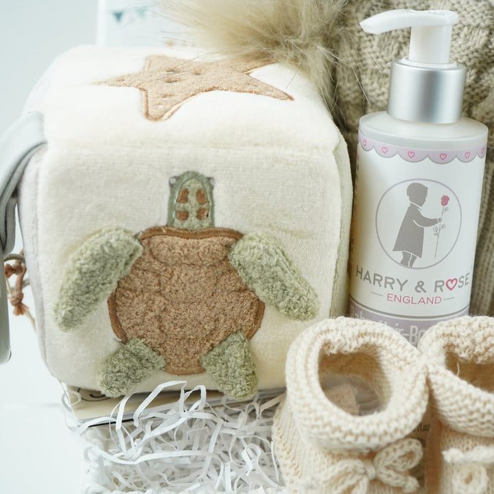 neutral baby hamper with baby dressing own, booties , baby journal, fluffy double pom pom hat, activity cube in neutral green, brown and cream with turtle, star fish and seahorse , soft turtle rattle toy