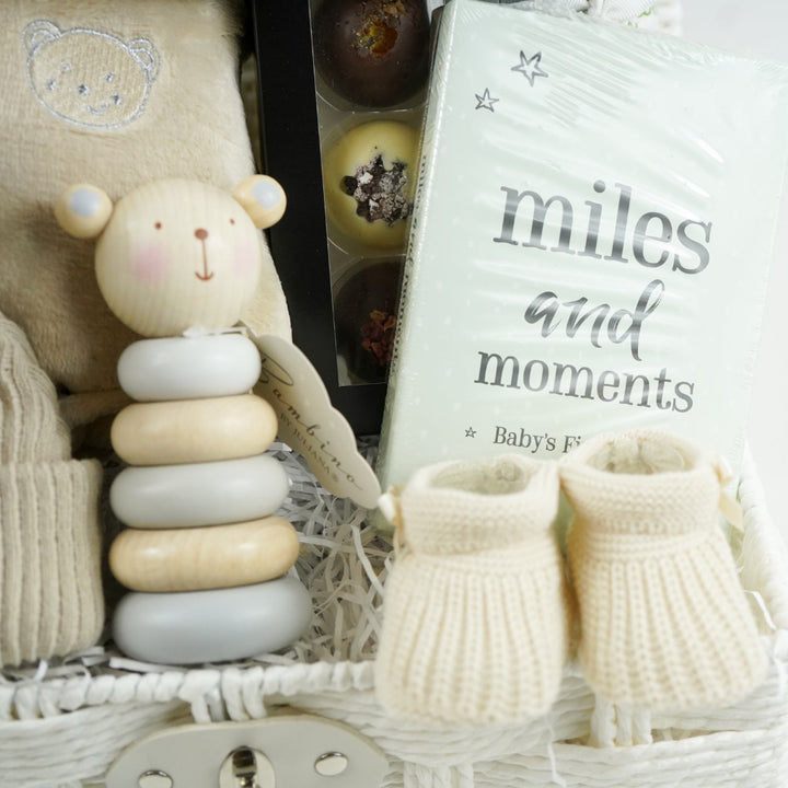 neutral baby gift with beige baby dressing gown, bamboo baby cellular blanket in beige, beige baby hat with teddy face, milestone baby cards, beige baby booties, wooden stacking toy,  chocolate