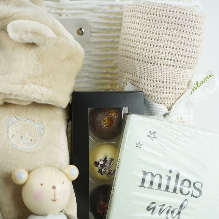 neutral baby and mum gift hamper includes neutral coloured baby dressing gown with cute ears, biscuit coloured baby pompom hat with teddy embroidery, wooden stacking toy, biscuit coloured baby booties, chocolates , milestone cards and bamboo cellular blanket