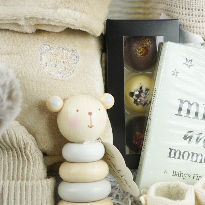 neutral baby gift with beige baby dressing gown, bamboo baby cellular blanket in beige, beige baby hat with teddy face, milestone baby cards, beige baby booties, wooden stacking toy,  chocolate