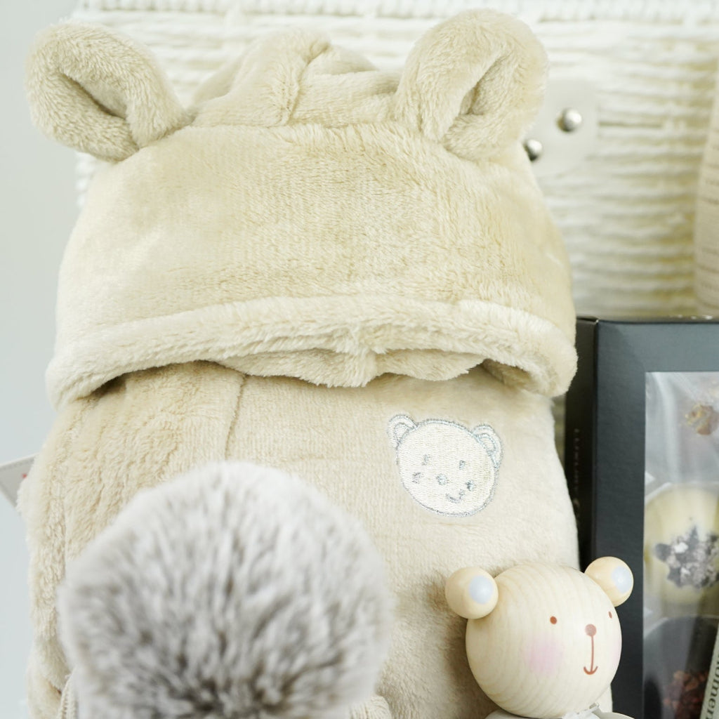 neutral baby gift with beige baby dressing gown, bamboo baby cellular blanket in beige, beige baby hat with teddy face, milestone baby cards, beige baby booties, wooden stacking toy,  chocolate