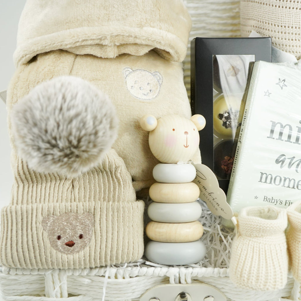neutral baby gift with beige baby dressing gown, bamboo baby cellular blanket in beige, beige baby hat with teddy face, milestone baby cards, beige baby booties, wooden stacking toy,  chocolate