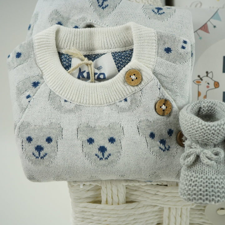 luxury baby gifts in white basket baby journal, organic baby blanket, organic snow bear baby romper, 2 pairs of baby booties, muslin, wooden staging toy and grey soft baby bear