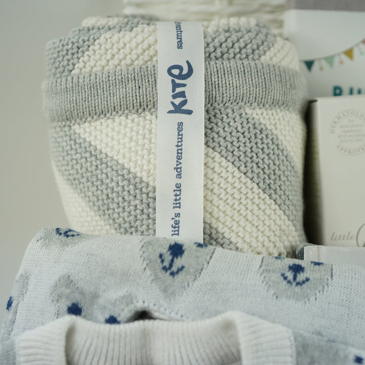 luxury baby gifts in white basket baby journal, organic baby blanket, organic snow bear baby romper, 2 pairs of baby booties, muslin, wooden staging toy and grey soft baby bear