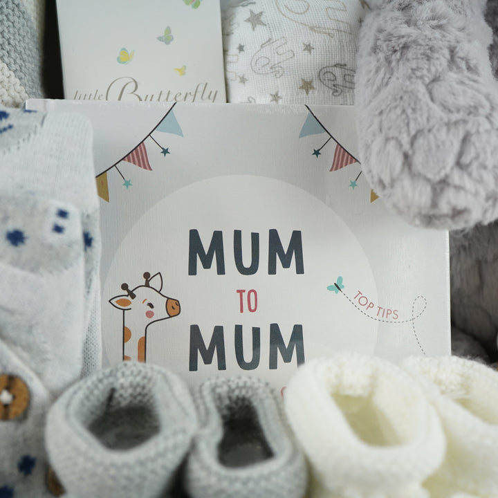 luxury baby gifts in white basket baby journal, organic baby blanket, organic snow bear baby romper, 2 pairs of baby booties, muslin, wooden staging toy and grey soft baby bear