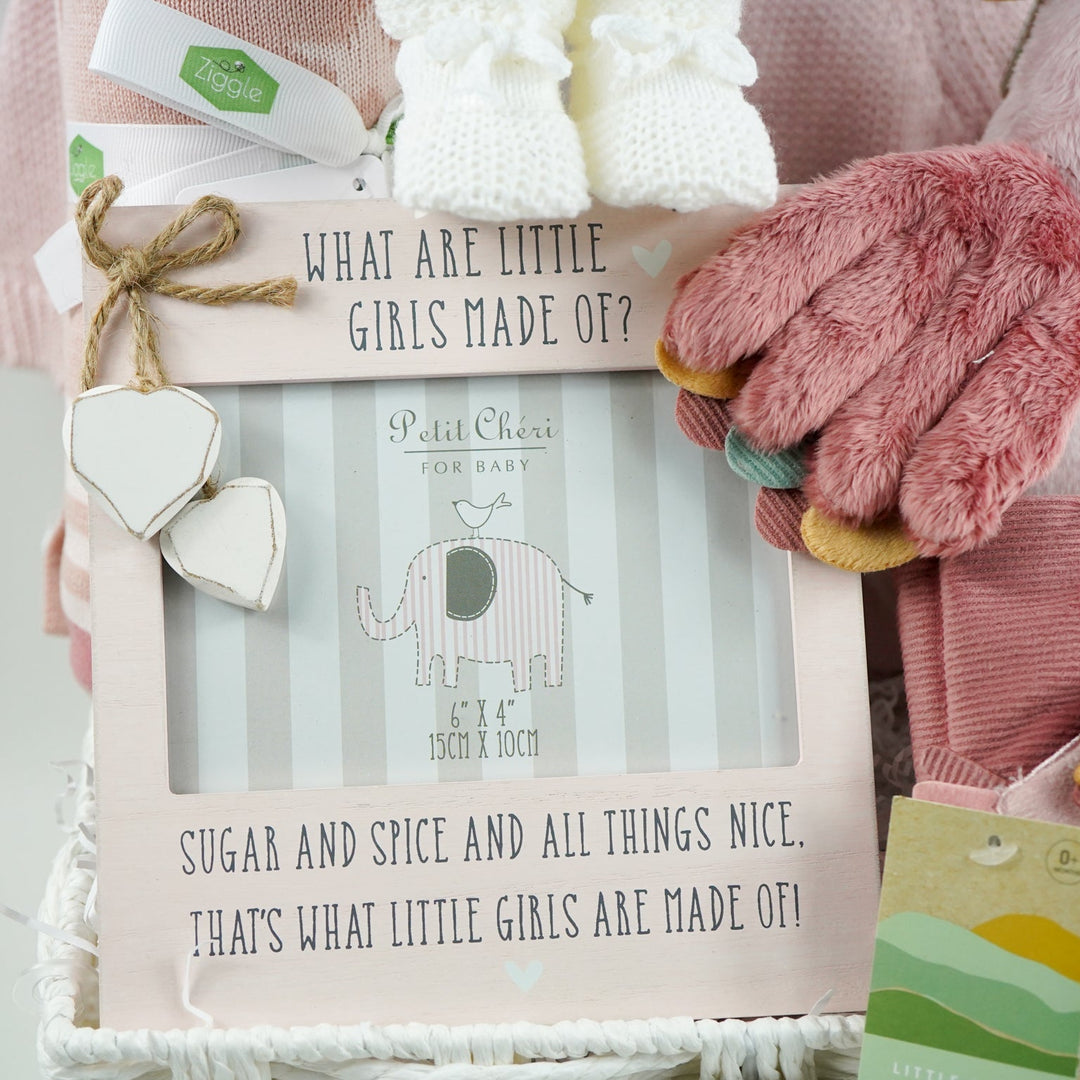 luxury baby girl hamper in mainly pink and white includes soft stroller book with a pink bird, butterflies and caterpillar theme, pink bird soft toy, white knit baby booties, dusky pink reversible baby blanket and pink baby girl picture frame and a pink baby girl cardigan in a white paper rope hamper basket