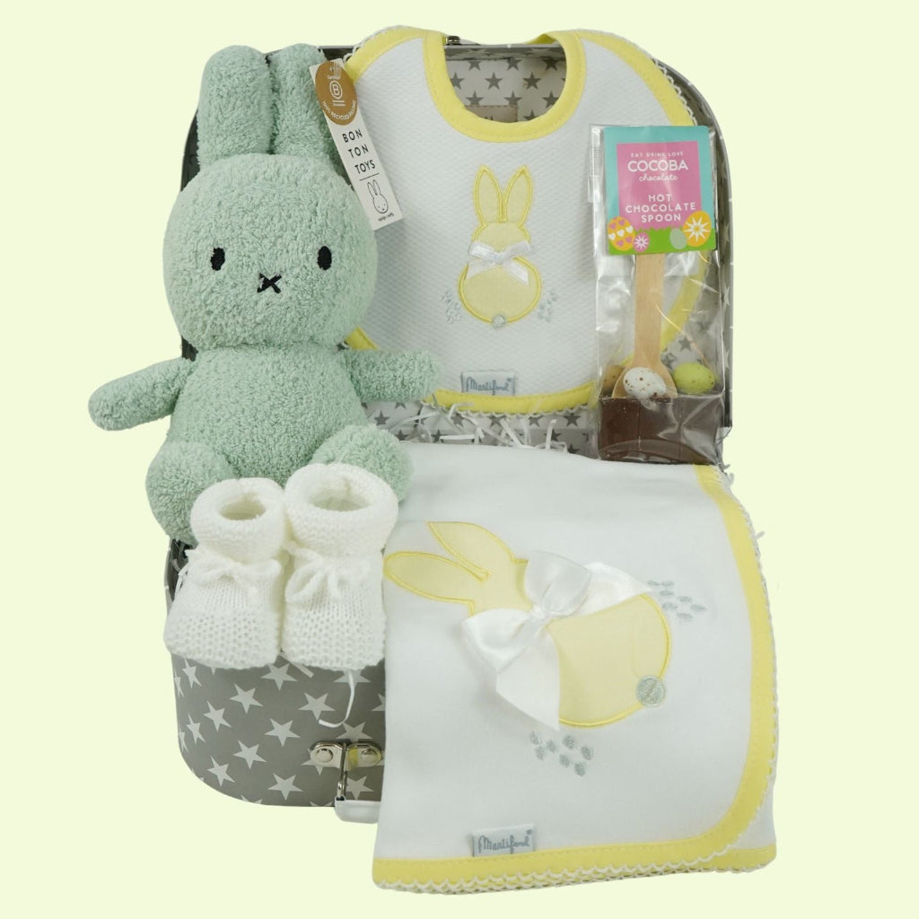 baby keepsake case with green miffy bunny, white bib with yellow scalloped edging and applique bunny with a bow and matching wrap, white baby knit booties , chocolate spoon with mini eggs