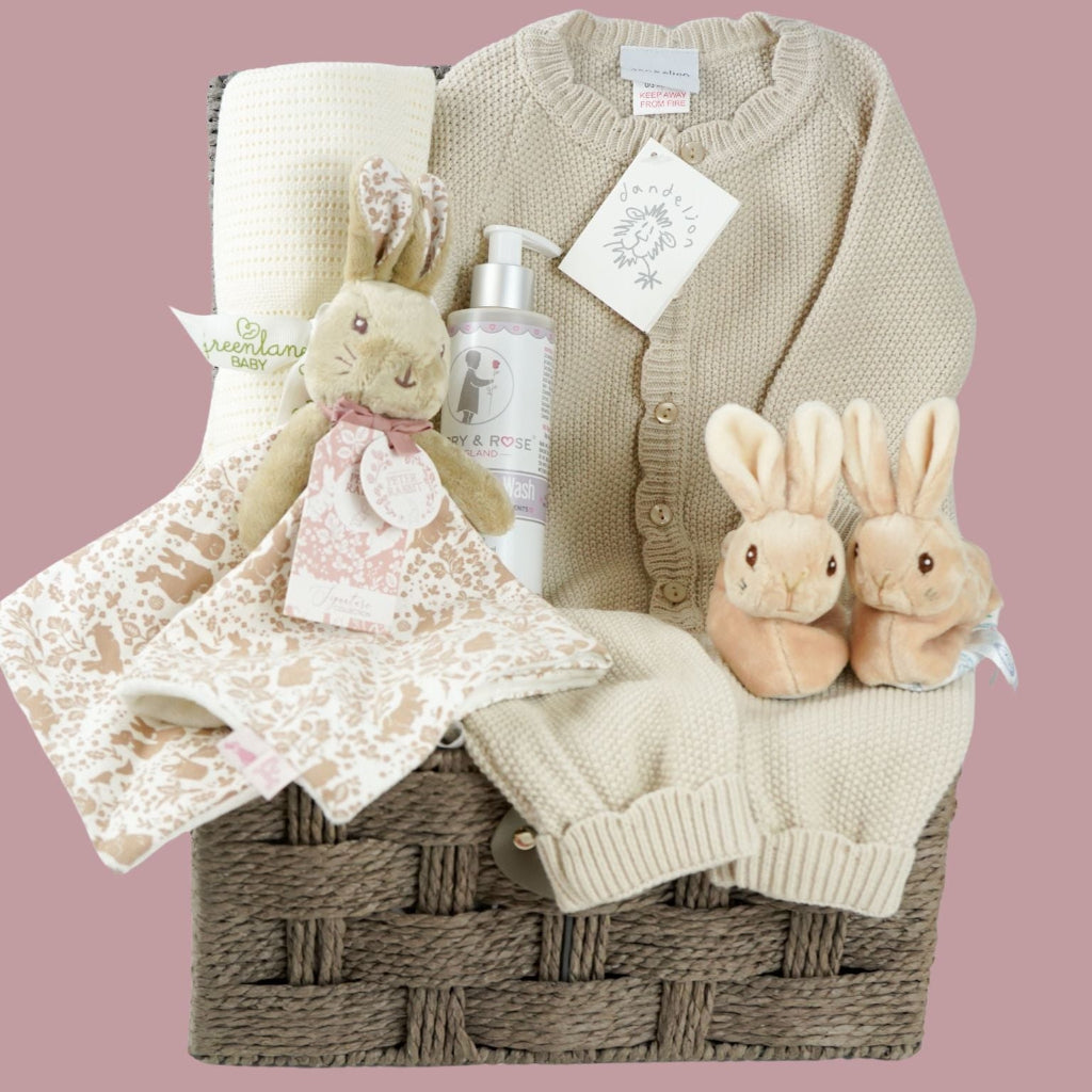 luxury baby girl hamper basket with taupe knitted romper with scalloped edges, cream cellular bamboo and cotton blanket, taupe and dusty pink flopsy bunny comforter , perter rabbit plush slippers , organic baby bubble bath